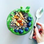 green smoothie in a bowl with blueberries, granola and chia seeds on top