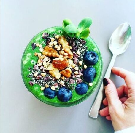 green smoothie in a bowl with blueberries, granola and chia seeds on top