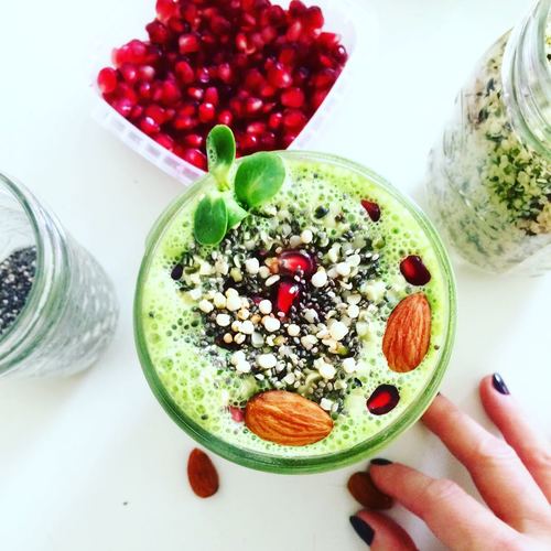 green smoothie in a bowl with pomegranate, granola and chia seeds on top