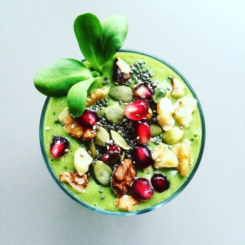 green smoothie in a bowl with pomegranate, granola and chia seeds on top