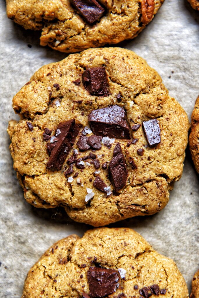 close up view of a freshly baked tahini chocolate chunk cookie with sea salt flakes by teri-ann carty