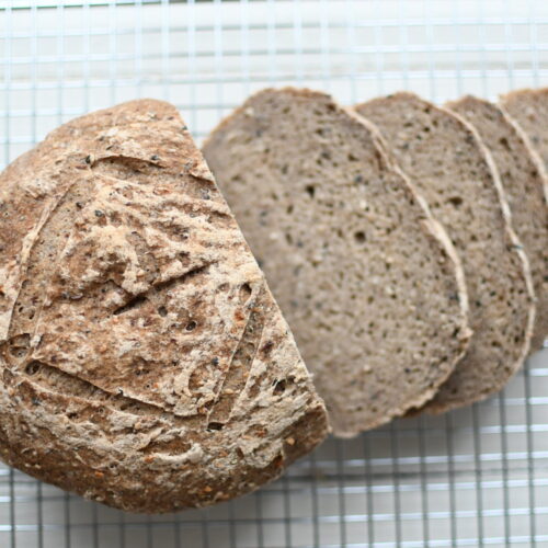 close up view of freshly baked seeded buckwheat flour sourdough bread with slices by teri-ann carty