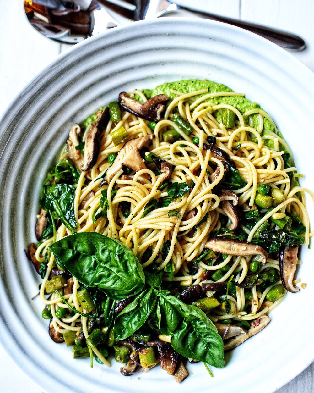 plate with spaghetti pasta, basil pea pesto sauce and large basil leaves as topping to decorate by teri-ann carty