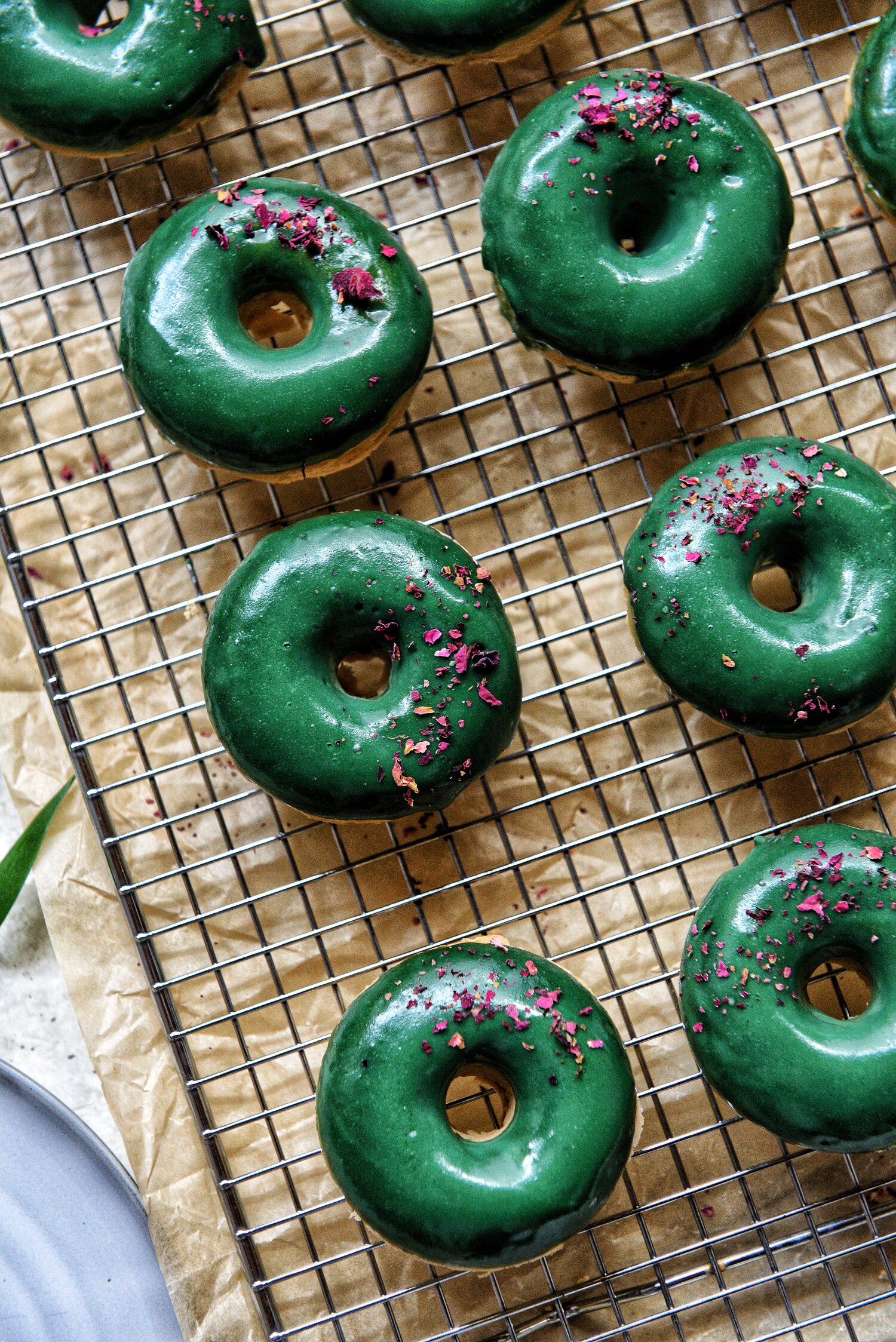 cooling rack with freshly baked, green glazed donuts and flakes of rose petals by teri-ann carty