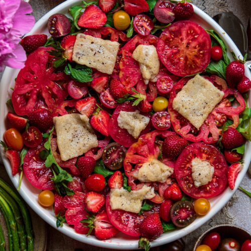beautiful bowl decorated with different shades of red fruit and vegetables with tomatoes and halloumi cheese by teri-ann carty