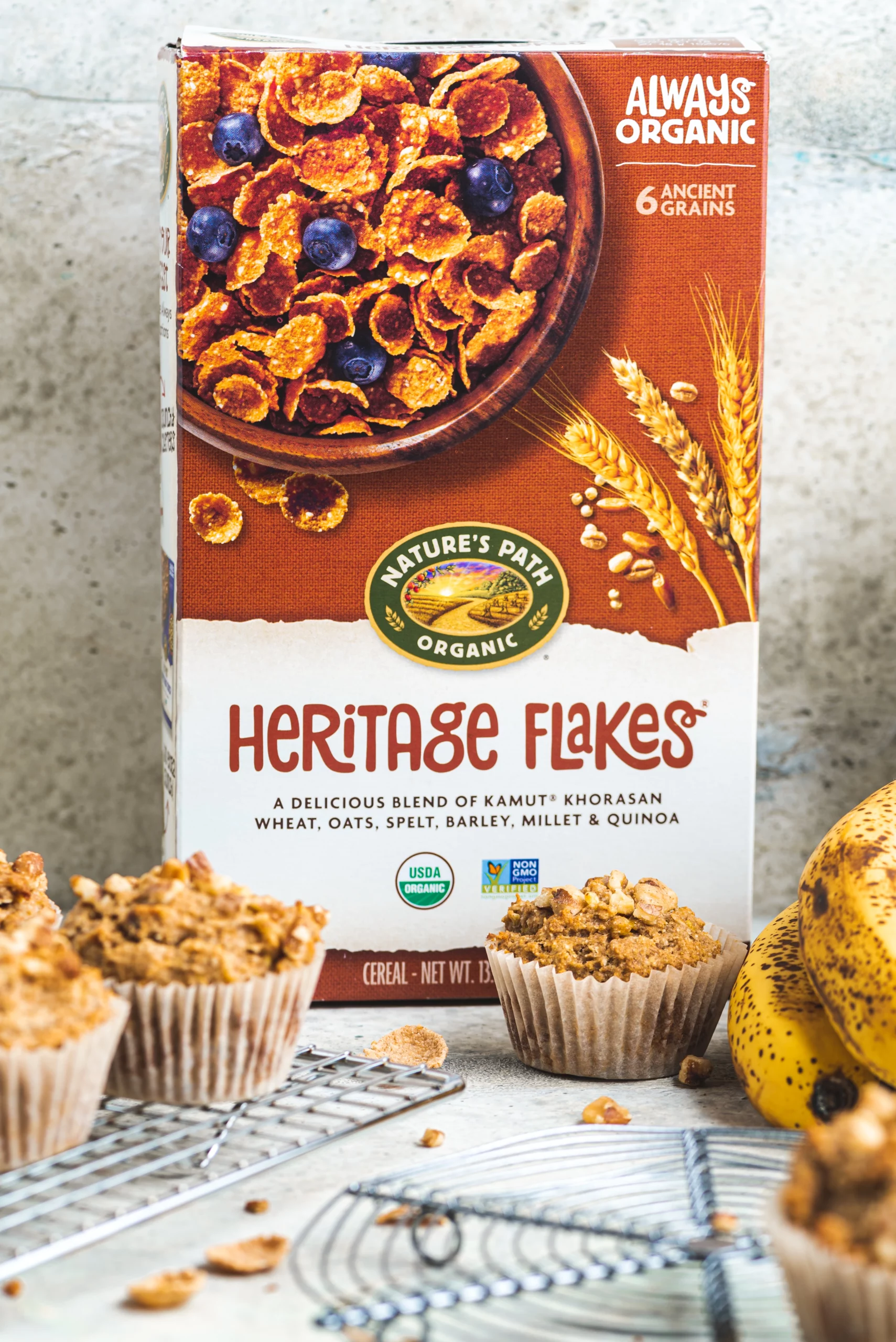 a box of heritage flakes cereal with a few muffins on cooling trays in front