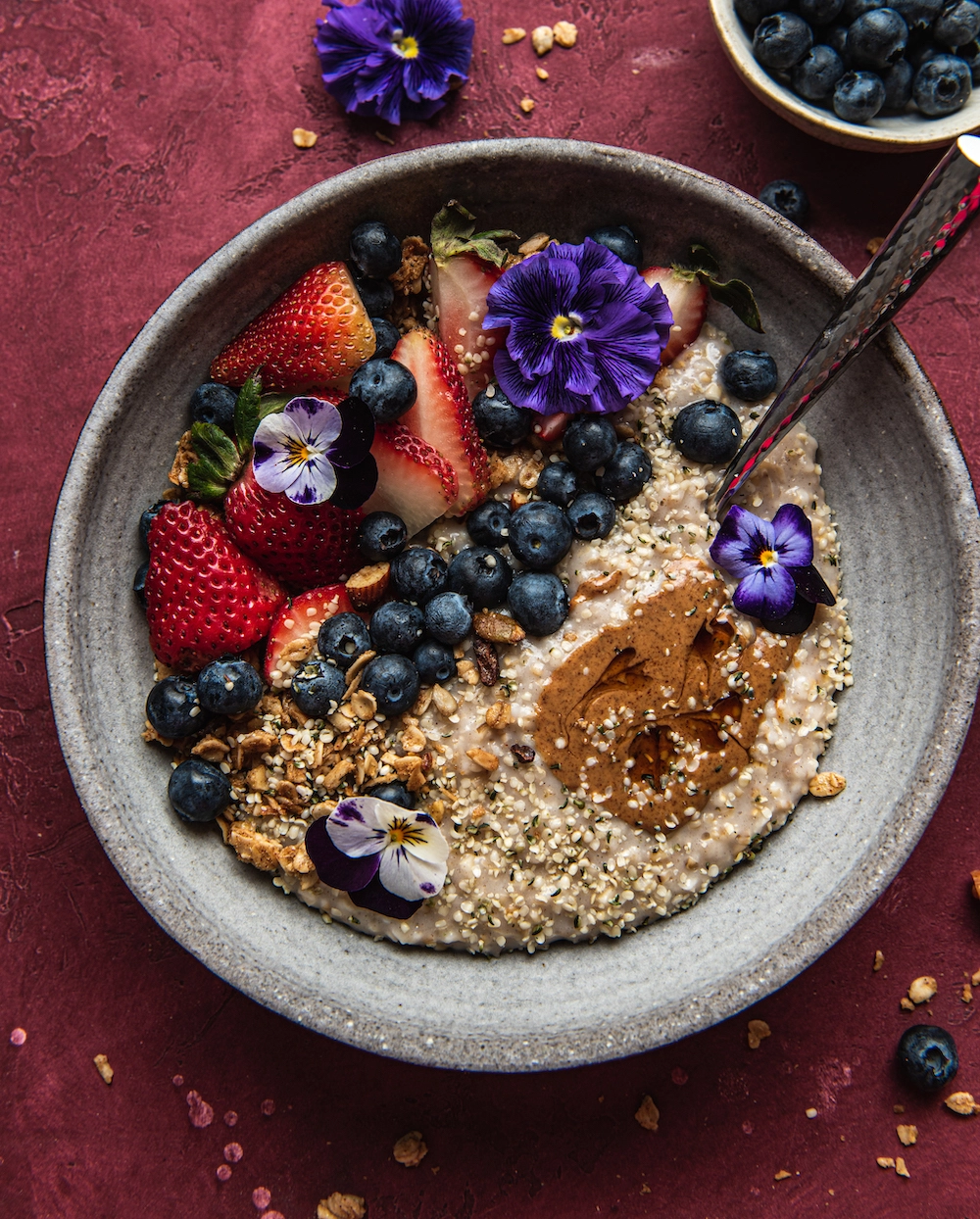 a beautiful ceramic bowl with steel cut oats, a sprinkle of seeds, blueberries and freshly sliced strawberries and edible purple flowers