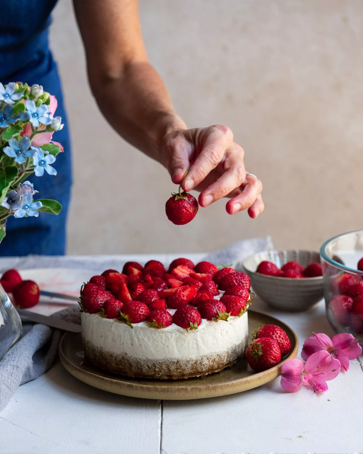 person putting decoration on cake. strawberry cheesecake