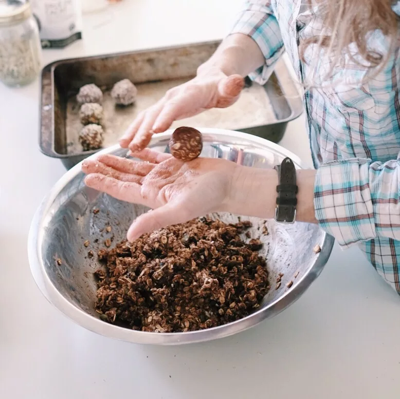 two hands rolling energy balls over a big metal bowl