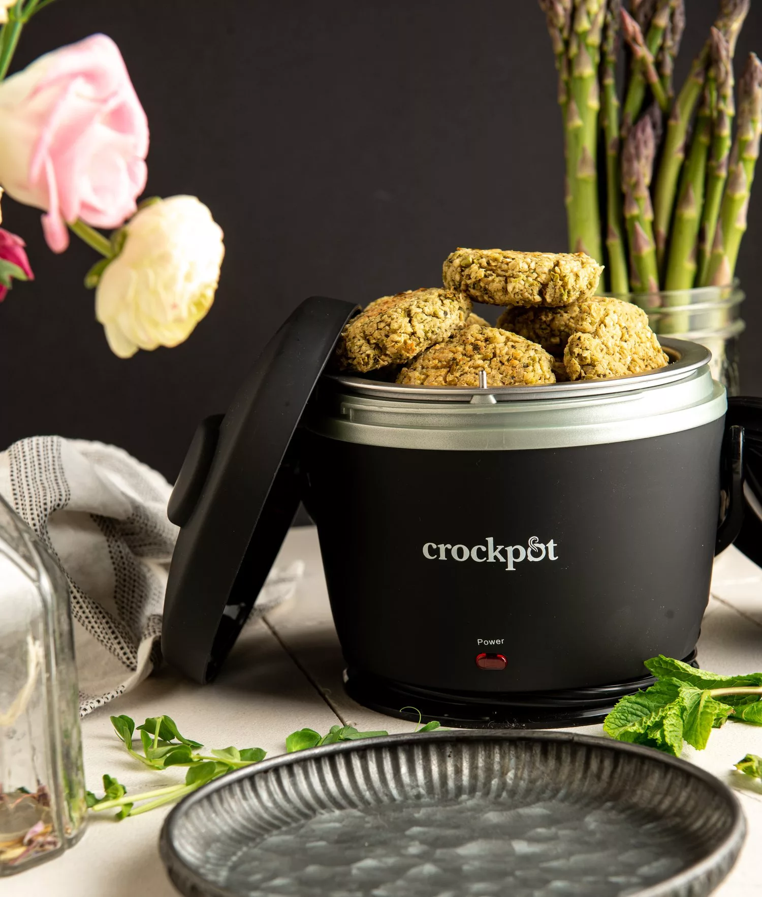 crockpot filled with white bean mint and green pea falafel patties. Roses and a cup of asparagus in the background
