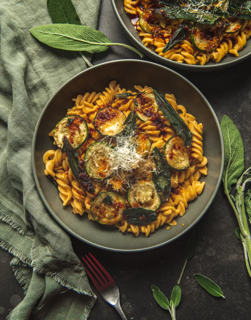 overhead view of creamy fusilli pasta with zucchini, sage leaves and finely grated parmesan cheese by teri-ann carty