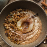 overhead view of grey bowl with oats, pear slice, cinnamon and baked homemade granola by teri-ann carty