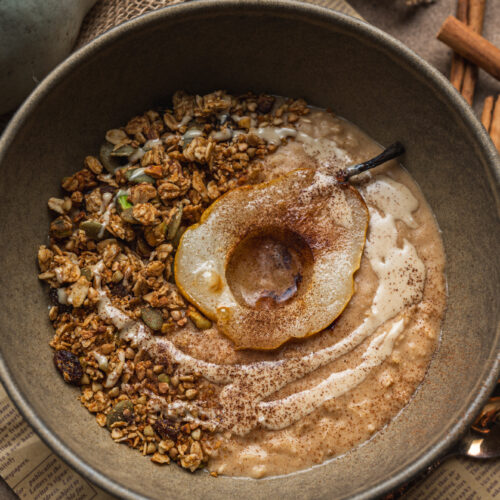 overhead view of grey bowl with oats, pear slice, cinnamon and baked homemade granola by teri-ann carty