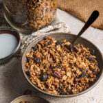 Bowl of gluten free granola by teri-ann carty. With a spoon and bowl of pecans