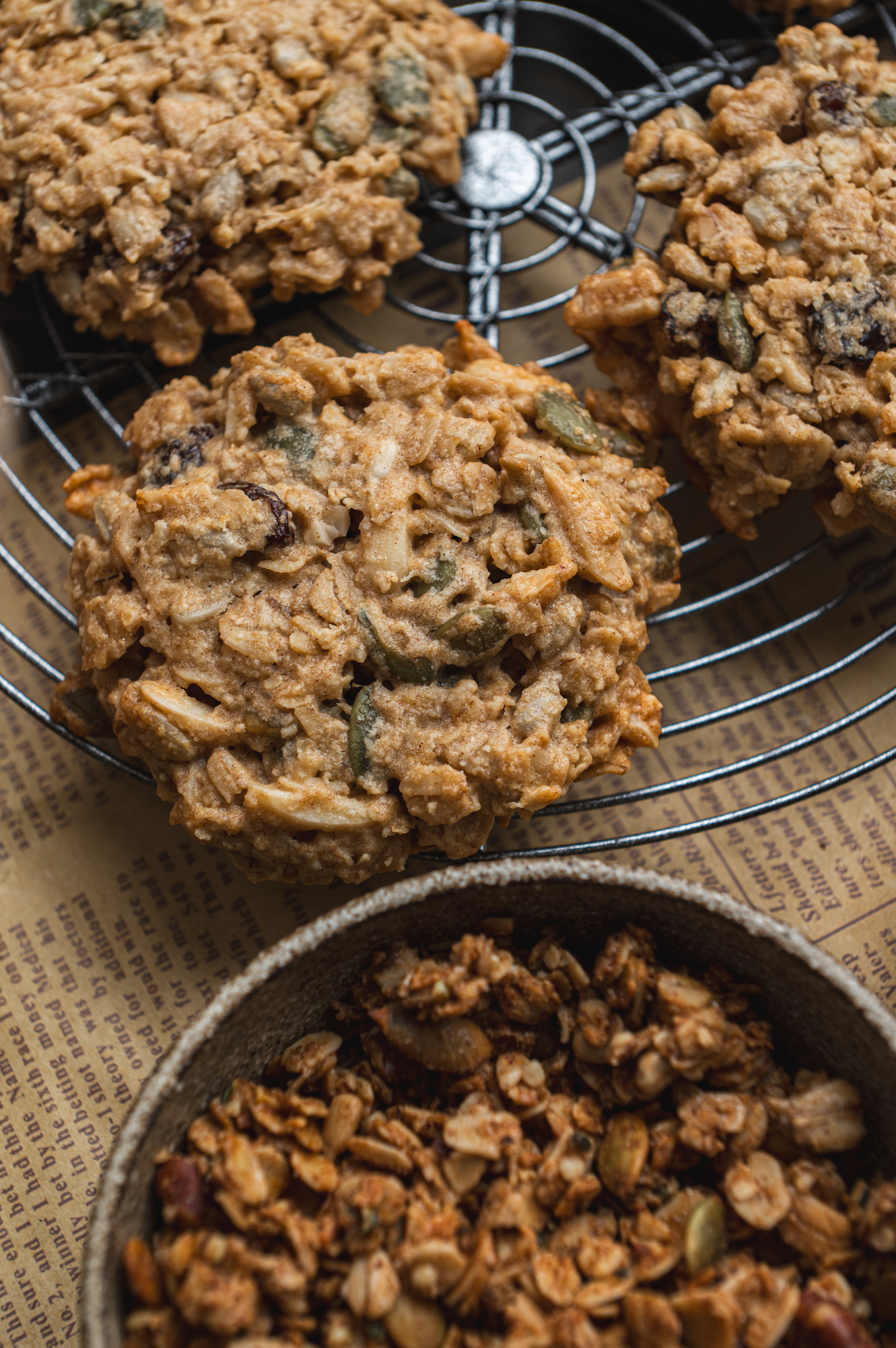 close up of freshly baked tahini granola cookies on a cooling rack and a small bowl of granola on the side by teri-ann carty