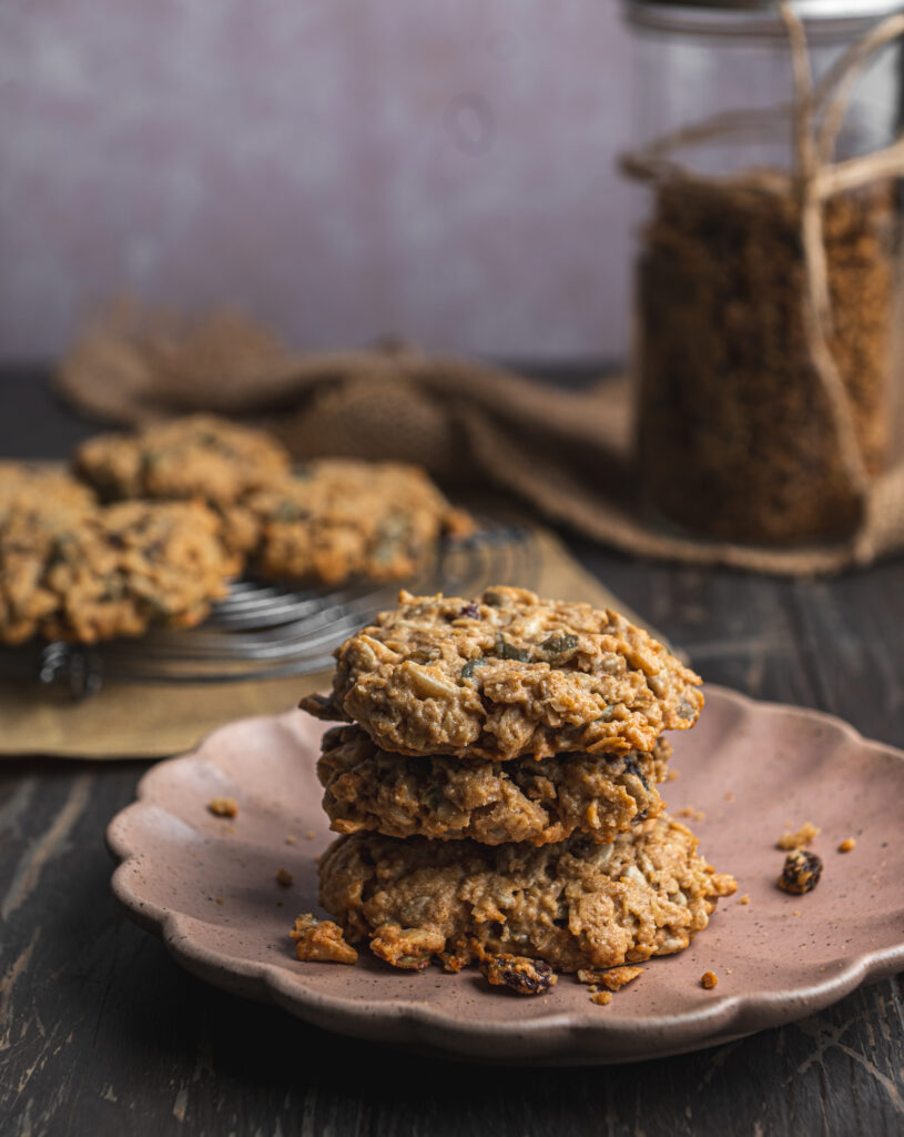 beautiful pink plate with three stacked baked tahini granola cookies and more cookies in the background by teri-ann carty