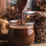 spoon filling a glass jar with freshly homemade chocolate nutella by teri-ann carty