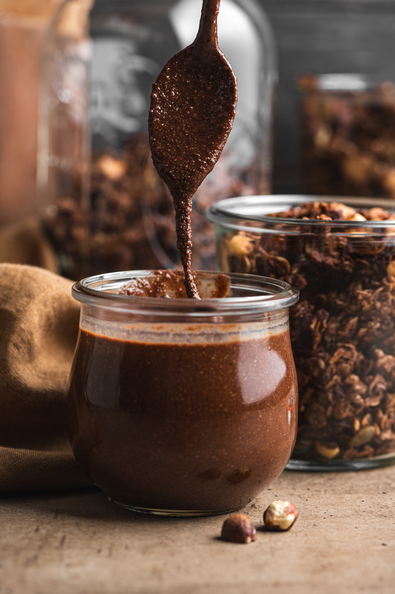 spoon filling a glass jar with freshly homemade chocolate nutella by teri-ann carty
