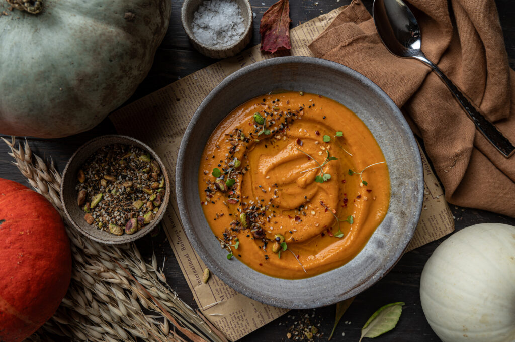 bowl with creamy pumpkin soup with seeds for topping and autumn themed background with brown tones by teri-ann carty