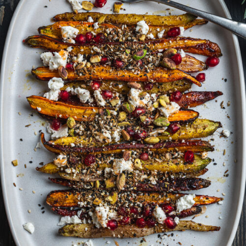 plate with freshly roasted carrots decorated with cheese and baked seeds by teri-ann carty