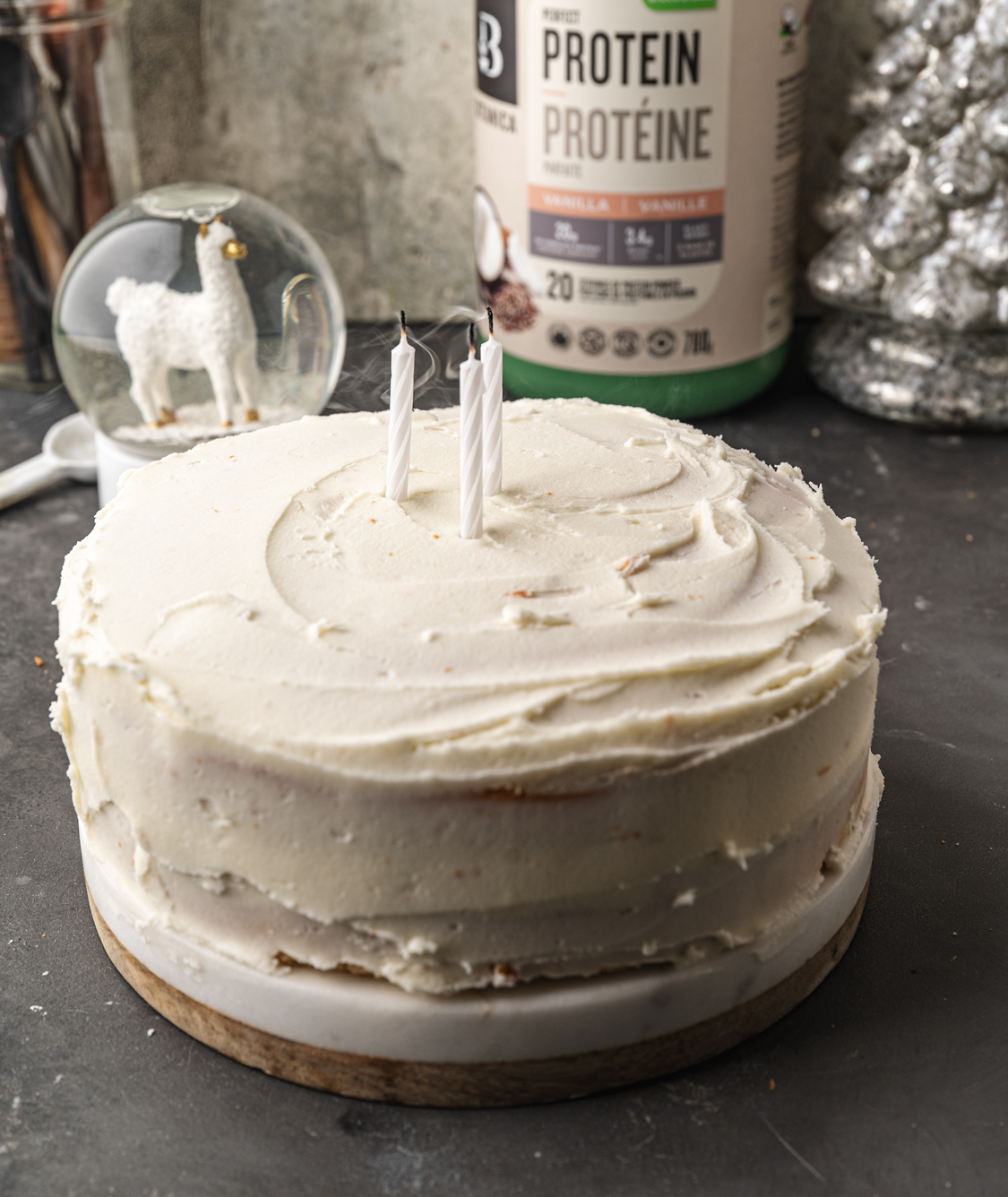 white frosted high protein birthday cake with three lit candles