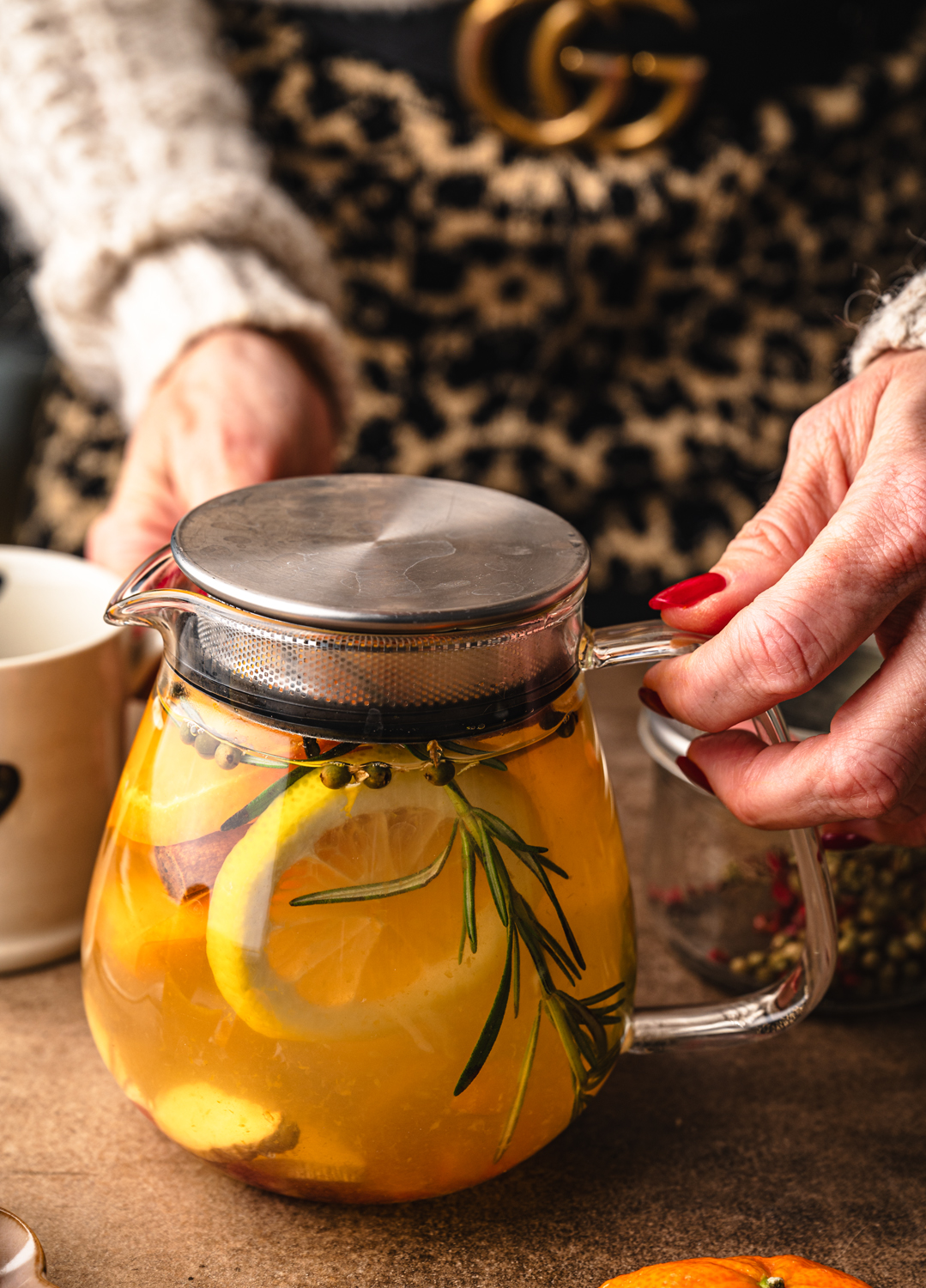 glass teapot filled with golden citrus tea, clementine, lemon, cinnamon and rosemary