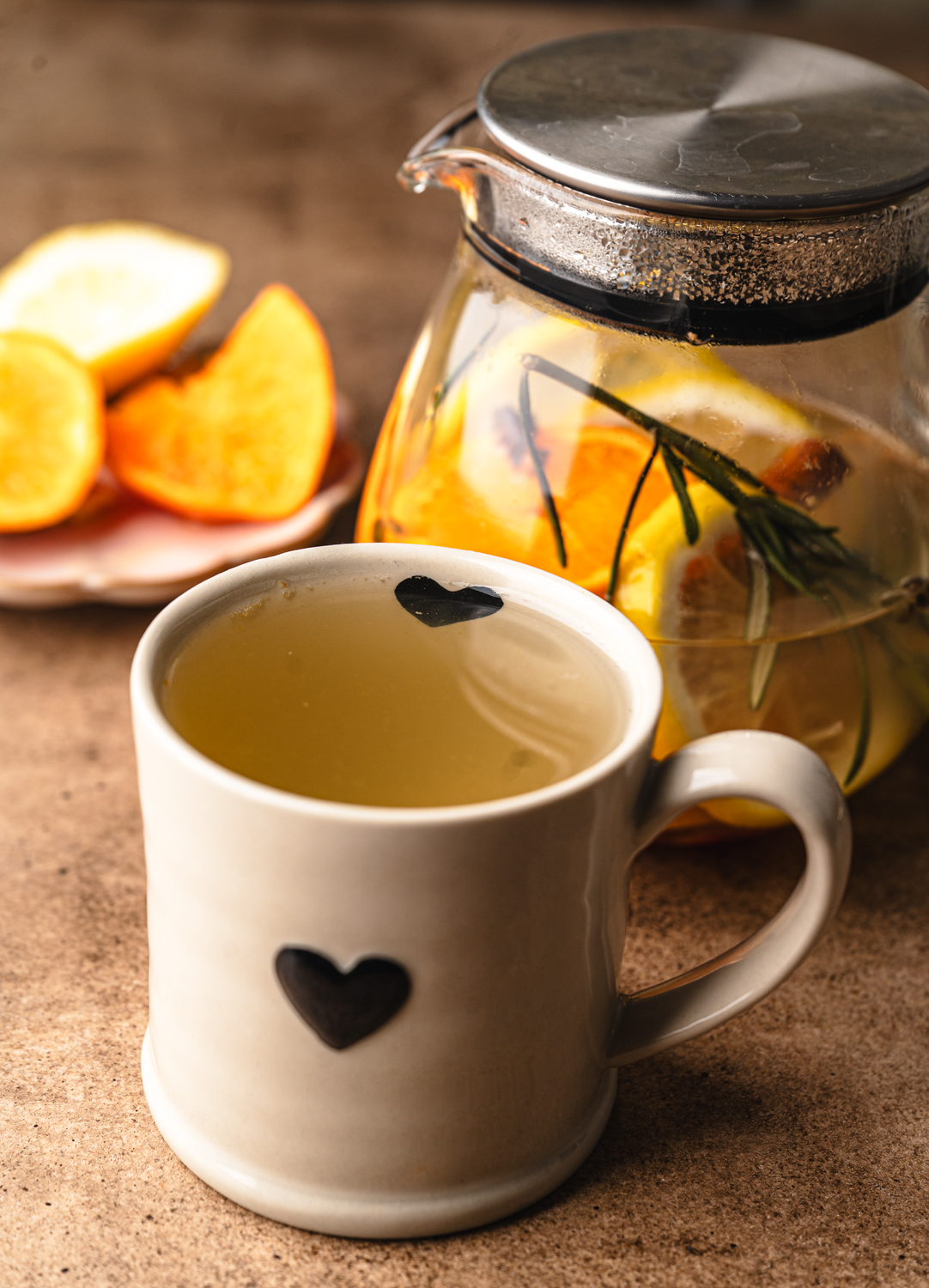 warm citrus tea served in a ceramic mug beside a glass teapot with lemon and rosemary