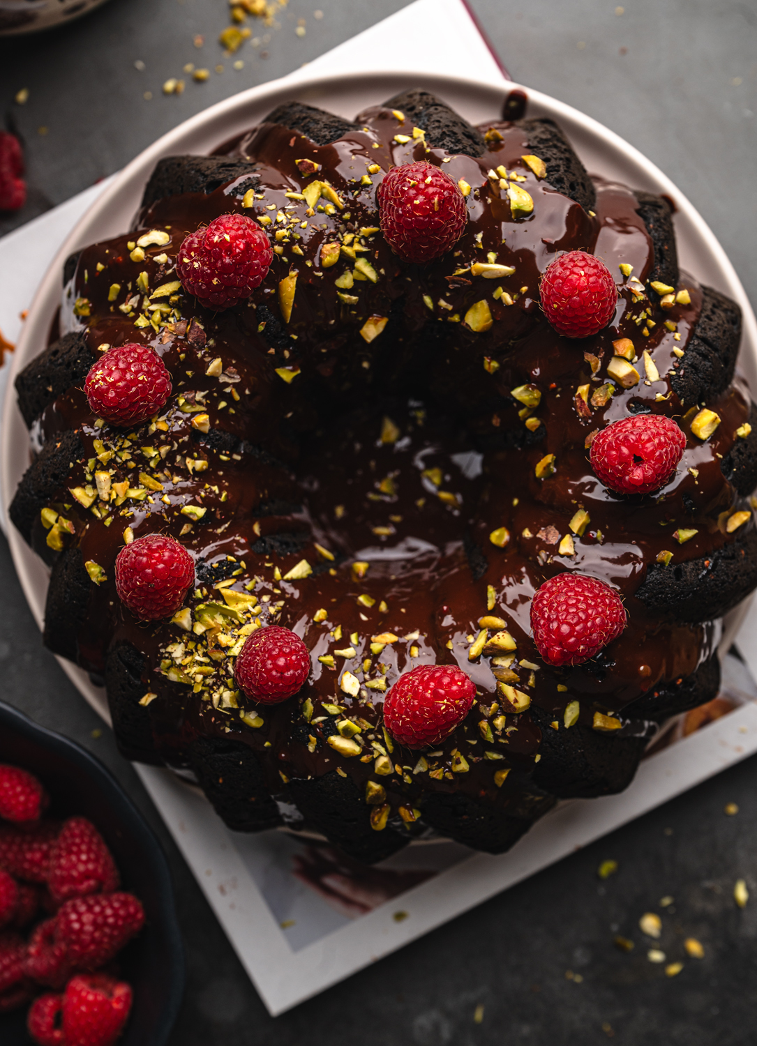 gluten-free raspberry chocolate bundt cake topped with chocolate glaze, fresh raspberries, and chopped pistachios