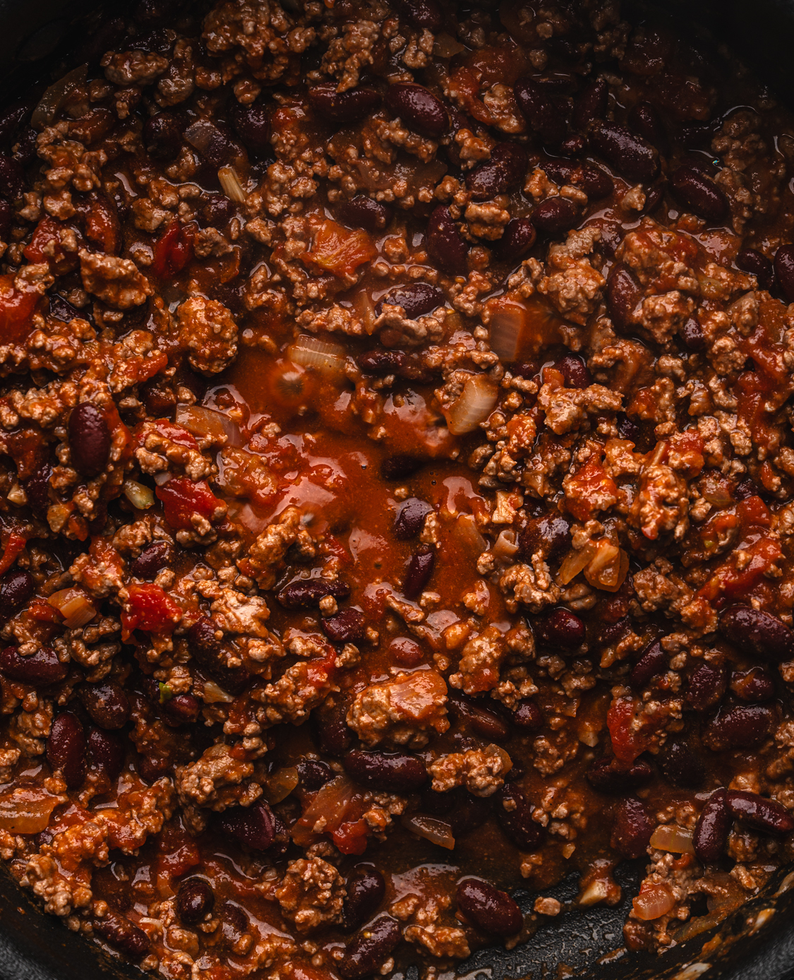 close up of beef and kidney bean chili with tomatoes and onions simmering in a skillet