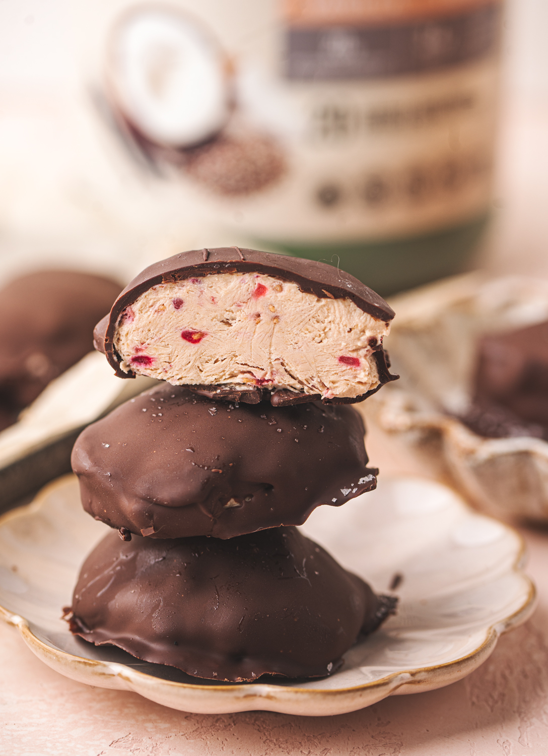 three yogurt bites stacked high covered in dark chocolate. the top yogurt bite is cut open to show the dairy free high protein inside with strawberry speckles