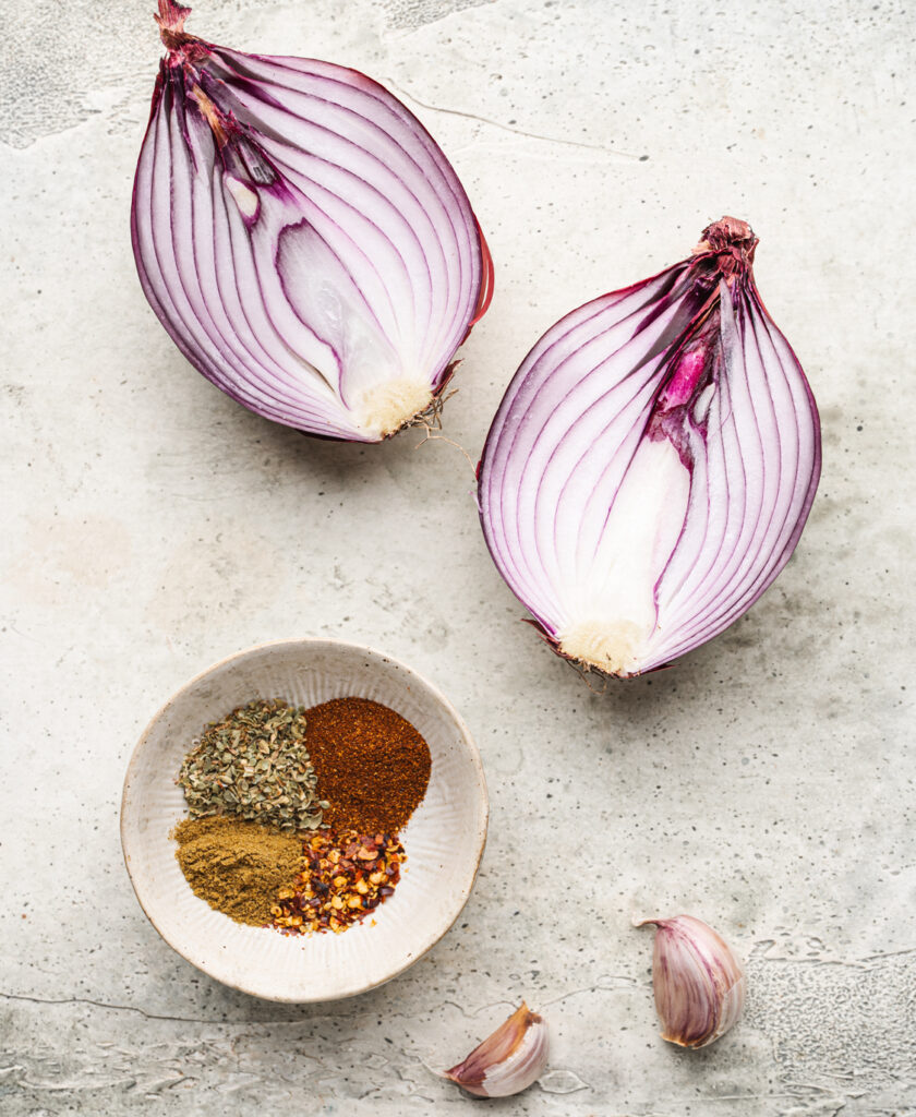 red onion split open and spices in a ramekin to make stuffed purple sweet potatoes