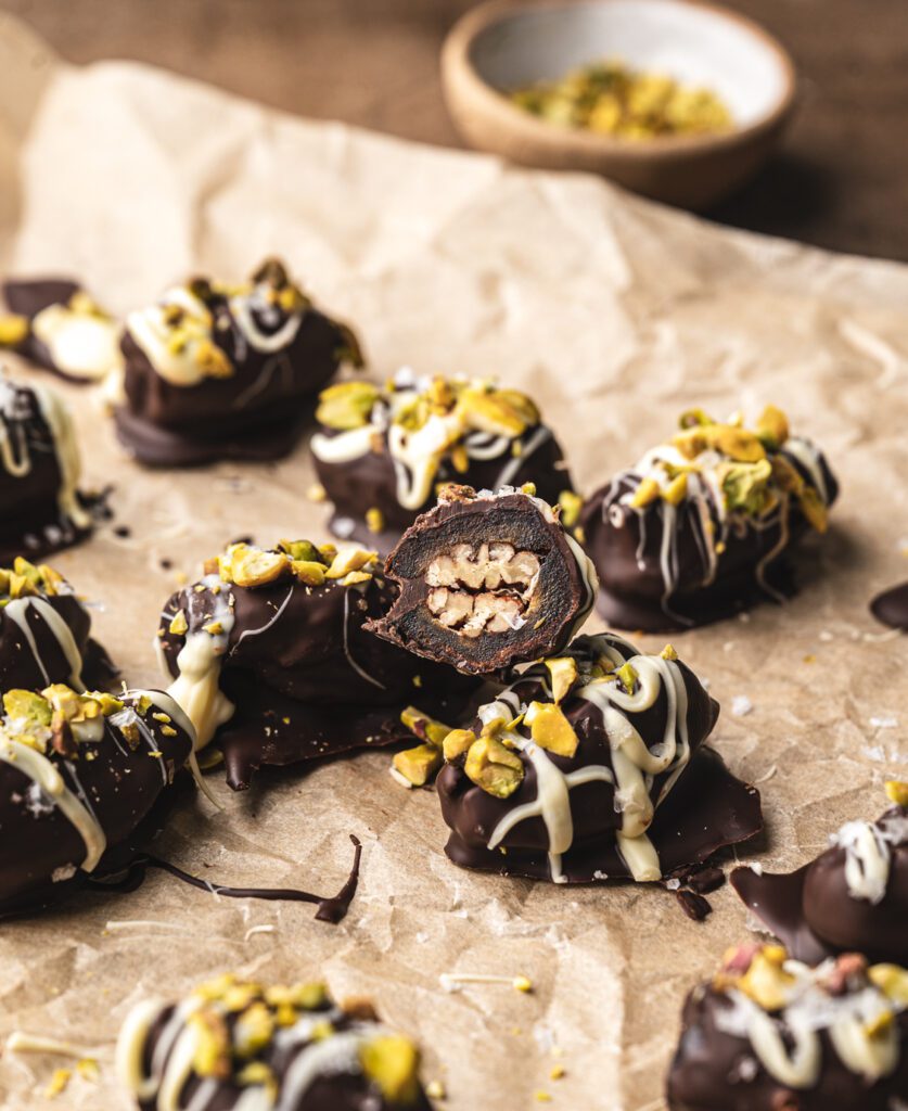 chocolate covered dates stuffed with pecans on a parchment paper, one stuffed date is sliced open showing the inside