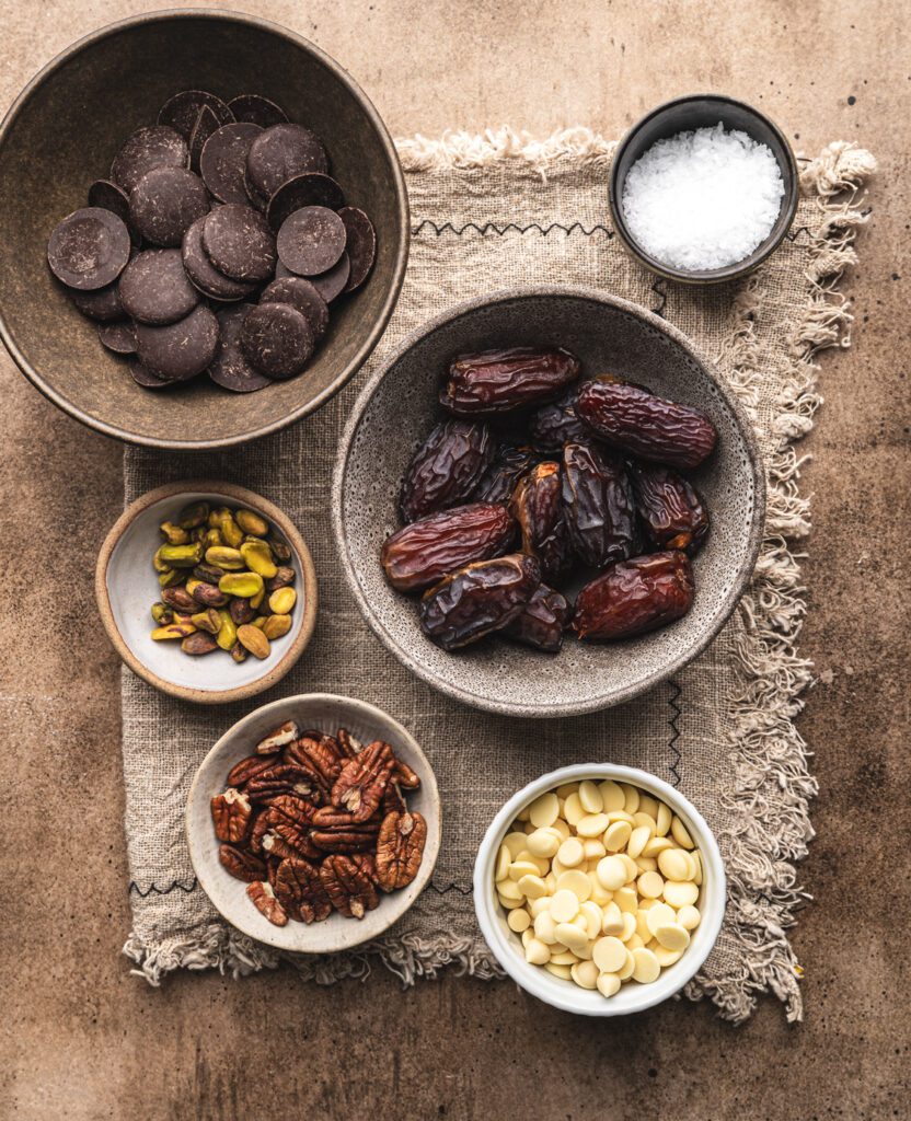 overhead view of several ceramic bowls filled with all the ingredients for pecan chocolate stuffed dates