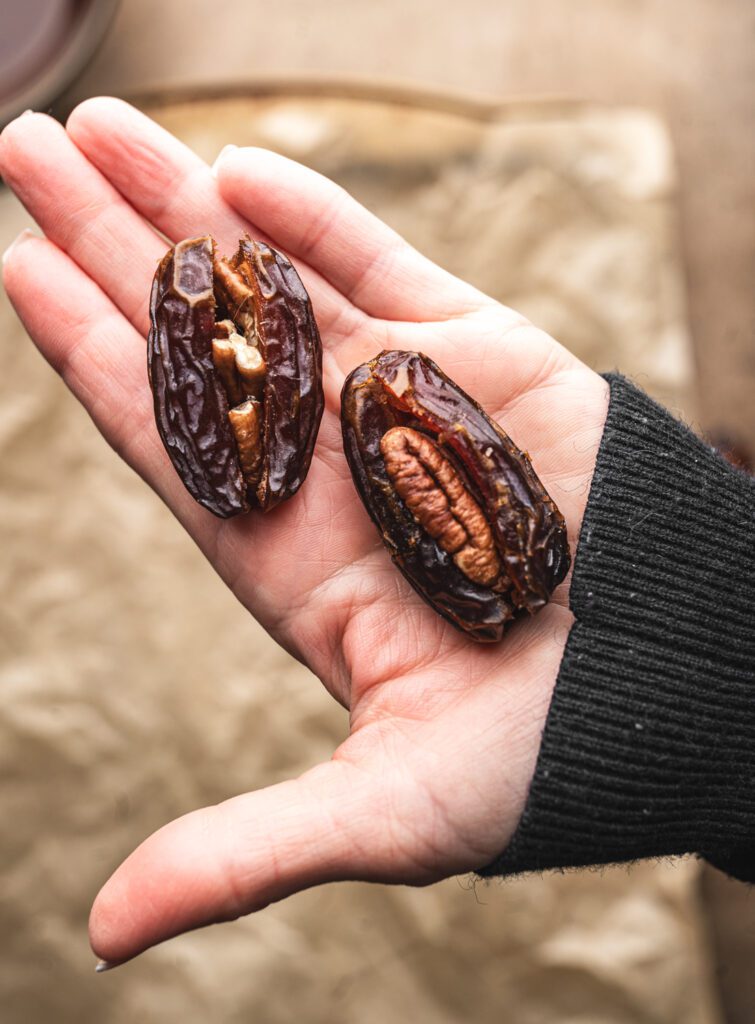 hand holding two dates that have been stuffed with pecans