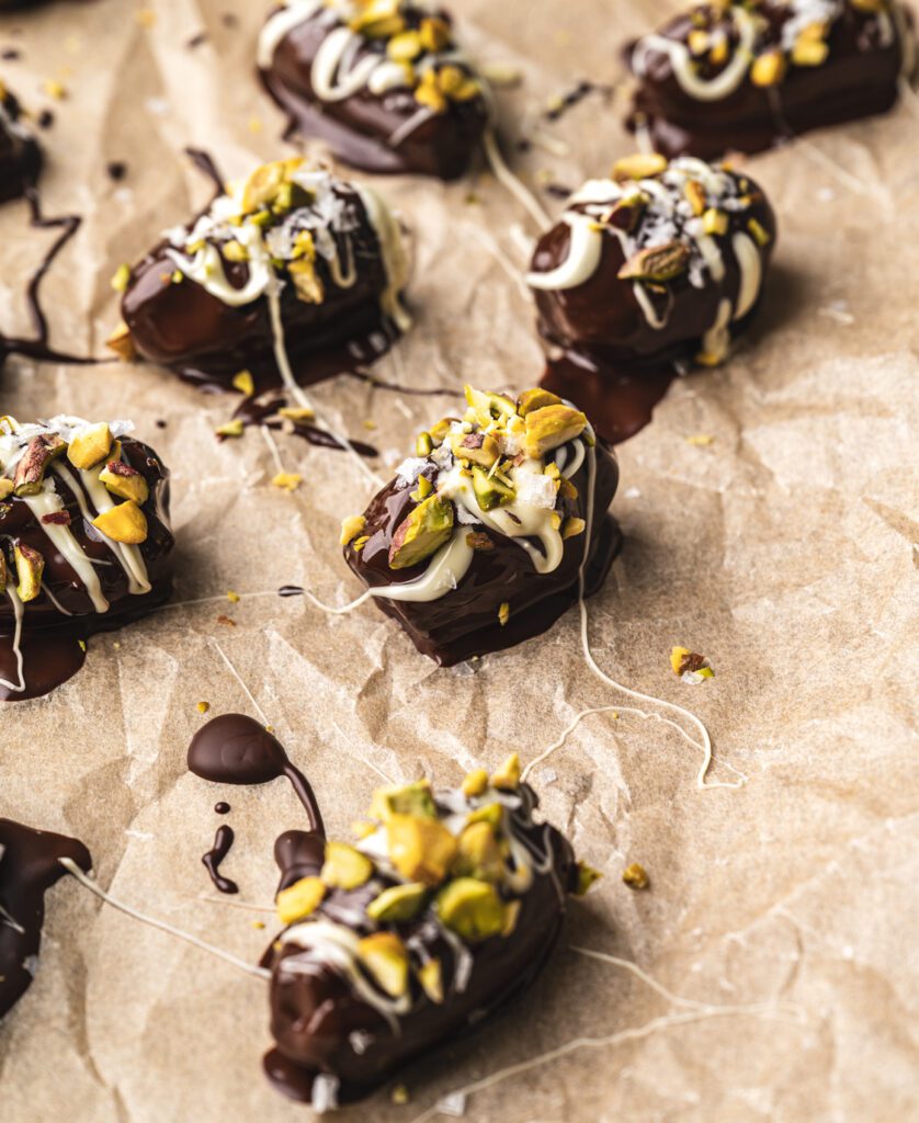 close up of freshly drizzled chocolate dipped stuffed dates with pistachio crumble and white chocolate