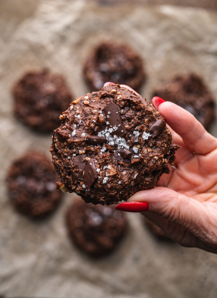 hand holding a flourless nutella cookie over the other nutella cookies on a baking tray