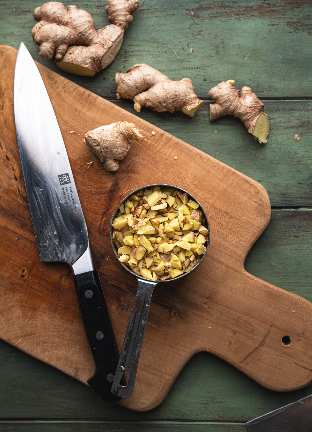 finely chopped fresh ginger measured beside a chef’s knife and whole ginger roots