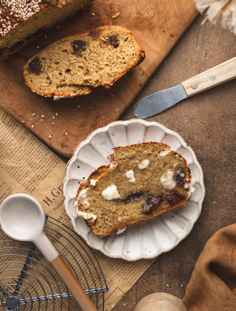 two slices of banana and date bread, one is on the cutting board and the other slice is on a white plate
