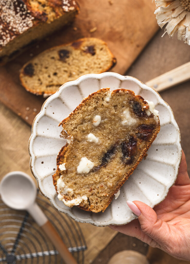 hand holding a plate with a slice of miso date and banana bread over the loaf of bread