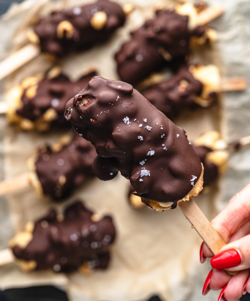 close up of banana popsicles covered in peanuts, chocolate, and flaked salt on top.