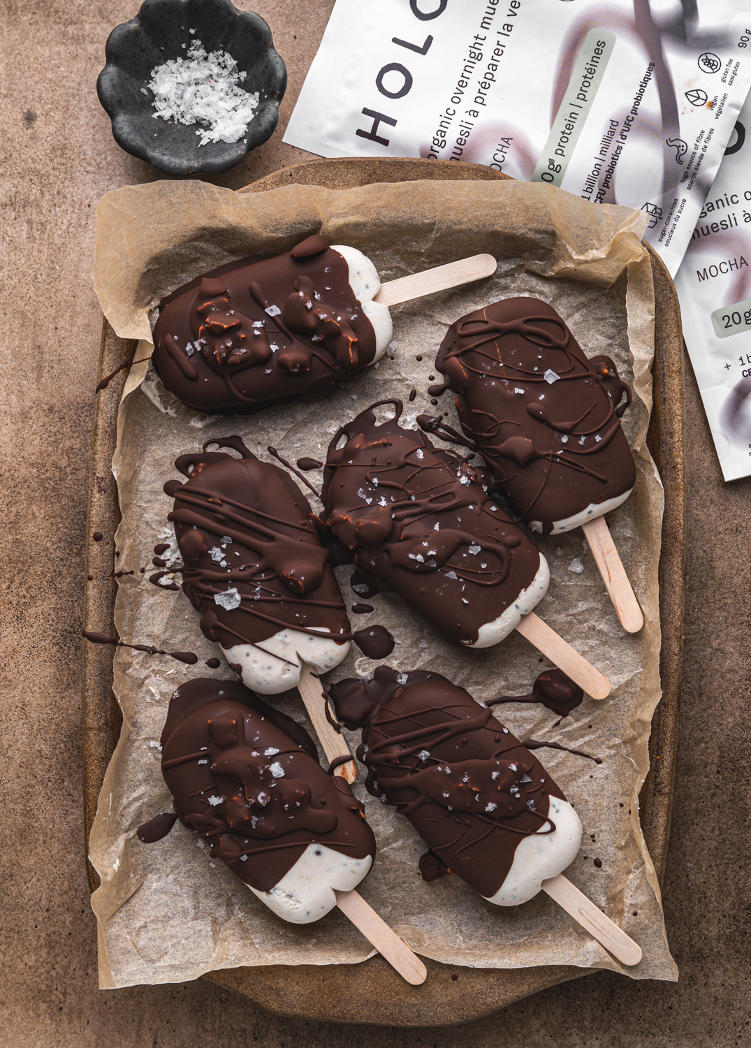 chocolate-covered mocha ice cream bars topped with flaky sea salt on a parchment-lined tray