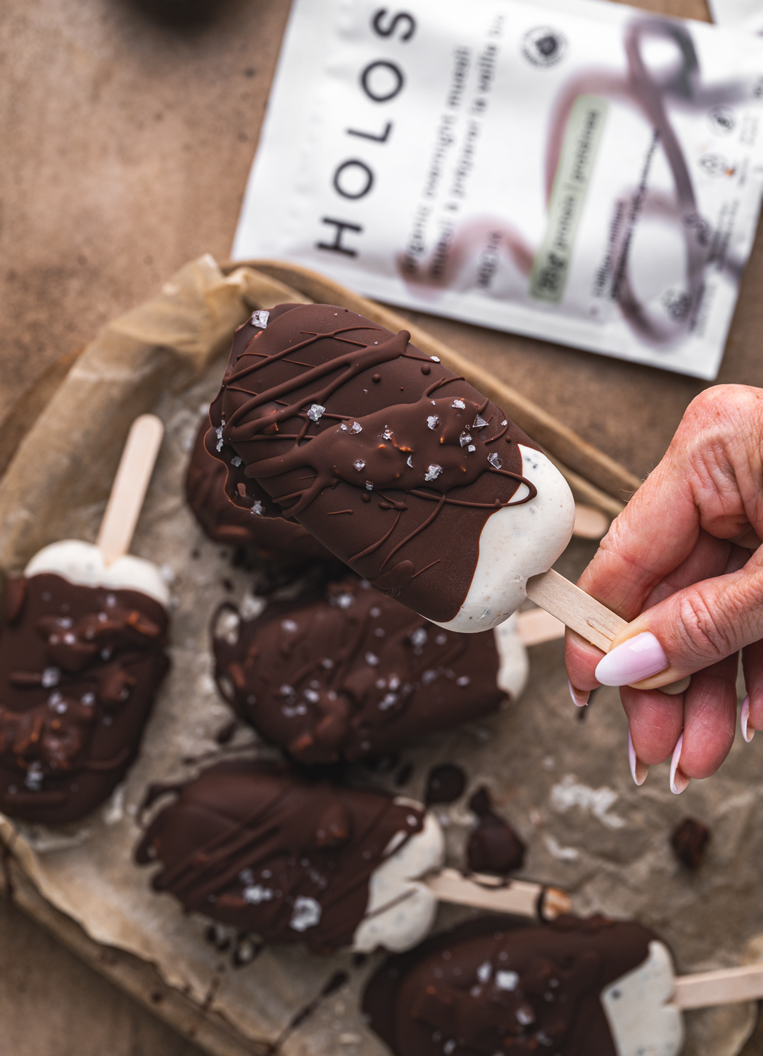 hand holding a chocolate-covered mocha ice cream bar topped with flaky sea salt
