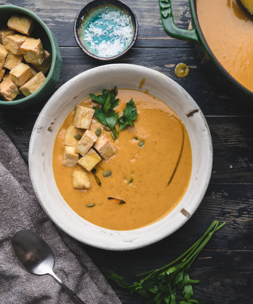 white rustic bowl filled with a creamy vegan carrot and sweet potato soup