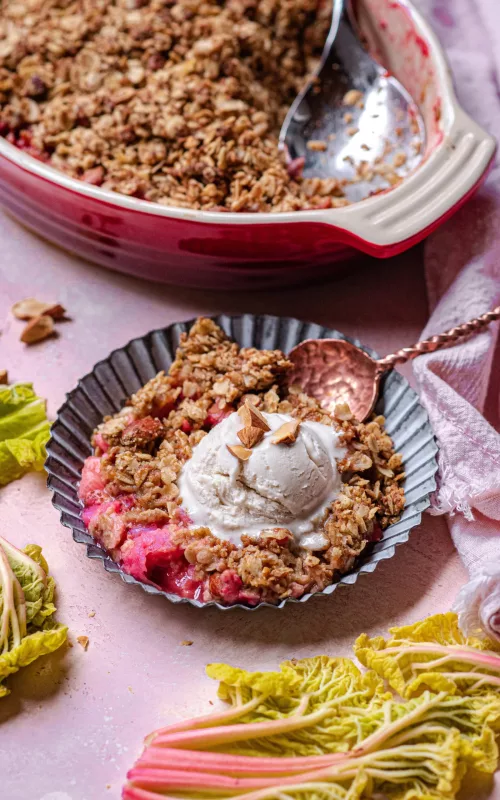 a metal scalloped bowl with strawberry rhubarb crisp and a scoop of vanilla ice cream