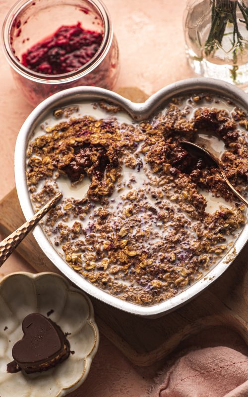 heart shaped bowl with baked homemade chocolate granola, planted based milk and silver spoons, healthy breakfast by Teri-Ann Carty