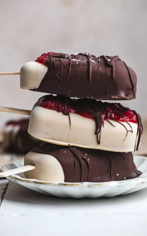 a stack of ice cream bars with strawberry jam oozing out of the chocolate dripped cover.