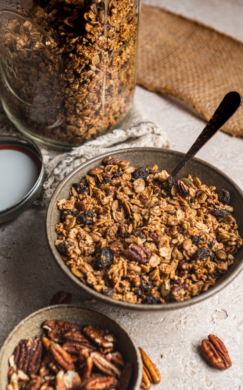 Bowl of gluten free granola by teri-ann carty. With a spoon and bowl of pecans